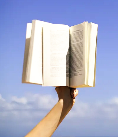 A hand holds a book up against the sky.