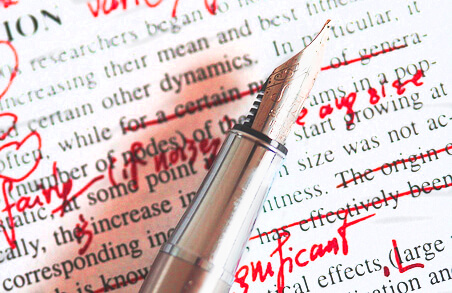 A silver pen sits on top of a printed page with red markup.