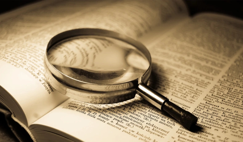 A magnifying glass sits on top of an open dictionary.